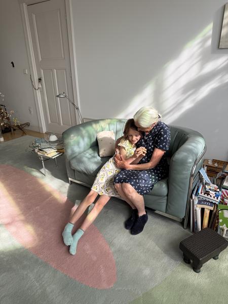 A heartwarming moment unfolds in a sunlit living room, where an older woman and a young girl share a tender embrace on a teal couch